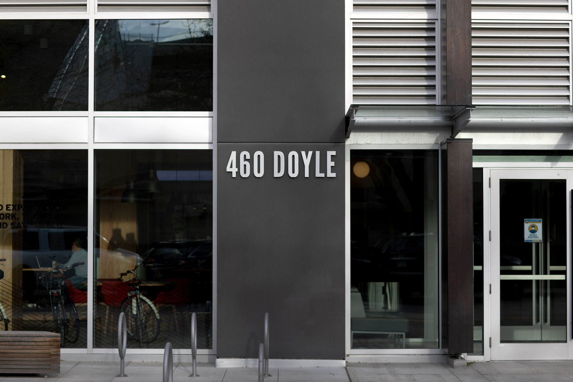 View of the side of a building with big glass windows and a grey column with "460 Doyle" written on it in white.